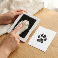 A dog's paw pressed onto the inkless pad beside the finished black paw print on a keepsake card